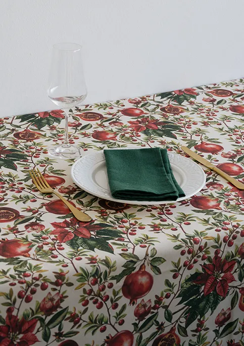 AYLON fabric, from GRENAT Collection. Tablecloth with SISMIC napkin. A bold botanical design featuring poinsettias and pomegranates. The red tones are more prominent here, giving the pattern a fuller and more decorative presence.